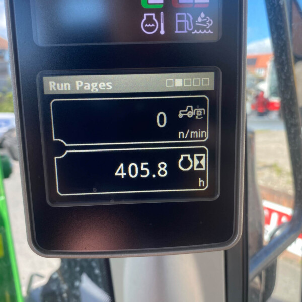 Close-up of a tractor dashboard showing 'Run Pages' and an hour meter reading (hours) with an outdoor background.