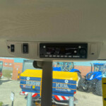 Inside a vehicle cabin with overhead controls and radio, view through windshield of a construction site outside.