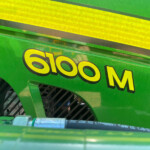 Close-up of a green industrial machine with yellow caution stripes and black lettering partially visible.