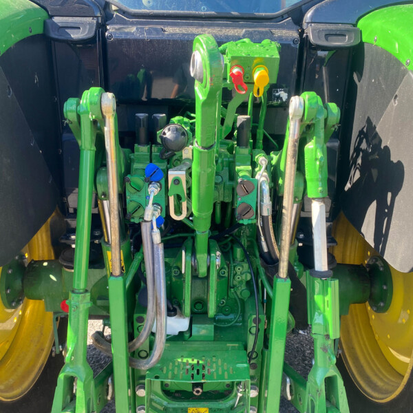 Rear tractor three-point hitch and hydraulic control levers in a green frame with yellow wheels; close-up of service connections and linkages.