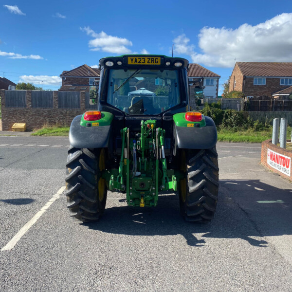 Back view of a green tractor in a residential street under a blue sky with white clouds.