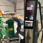 Digital tractor cockpit display showing 0 mph and 0 r/min with red warning icon, in a green agricultural machine cabin.