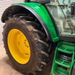 Close-up of a green tractor with a large muddy tire and bright yellow rim, plus green steps leading to the cab.