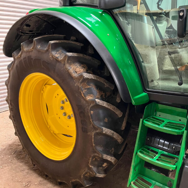 Close-up of a green tractor with a large muddy tire and bright yellow rim, plus green steps leading to the cab.