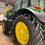 Close-up of a large green tractor front wheel with a yellow rim inside a shed.