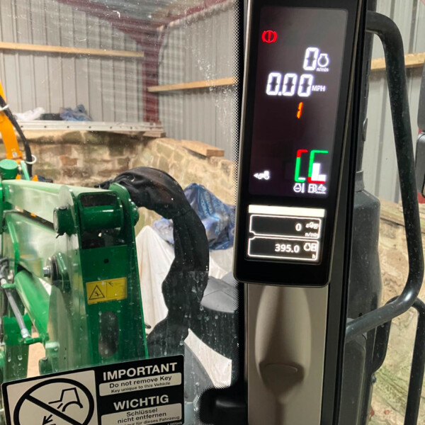 Digital tractor cockpit display showing 0 mph and 0 r/min with red warning icon, in a green agricultural machine cabin.