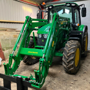 Green John Deere tractor with a front loader attachment inside a shed, large mud-covered tires and an orange beacon on top.