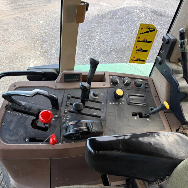 Interior of a tractor cab showing the control panel with multiple levers and a yellow instruction sticker near the window.