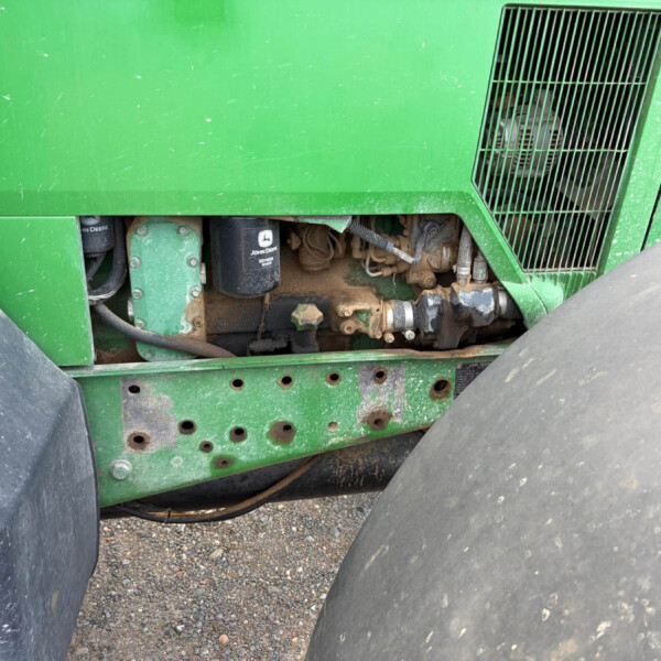Side view of a green John Deere tractor/harvester showing engine housing and exposed components under the paneling.