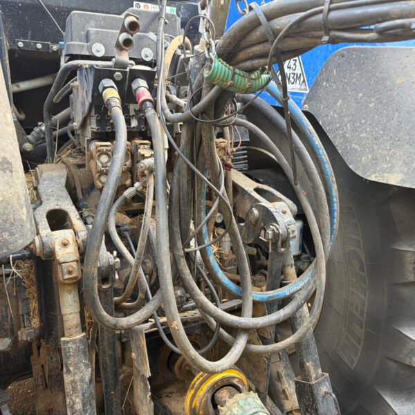 Close-up of dirt-covered hydraulic hoses and metal fittings on a heavy construction machine beside a large tire.