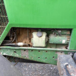 Close-up of a green agricultural machine showing an exposed engine, wiring, and a large black tire below.