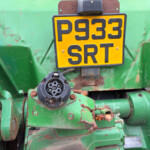 Close-up of a green agricultural machine with a yellow plate showing the numbers 9533 SRT and a circular connector nearby.