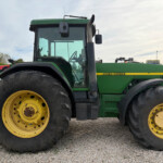 Close-up side view of a green John Deere tractor with large yellow wheels on a gravel lot.