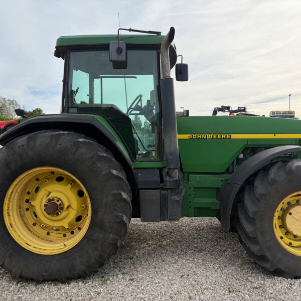 Close-up side view of a green John Deere tractor with large yellow wheels on a gravel lot.