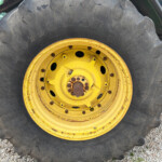 Close-up of a large tractor tire with a yellow rim, muddy tread, on gravel surface.