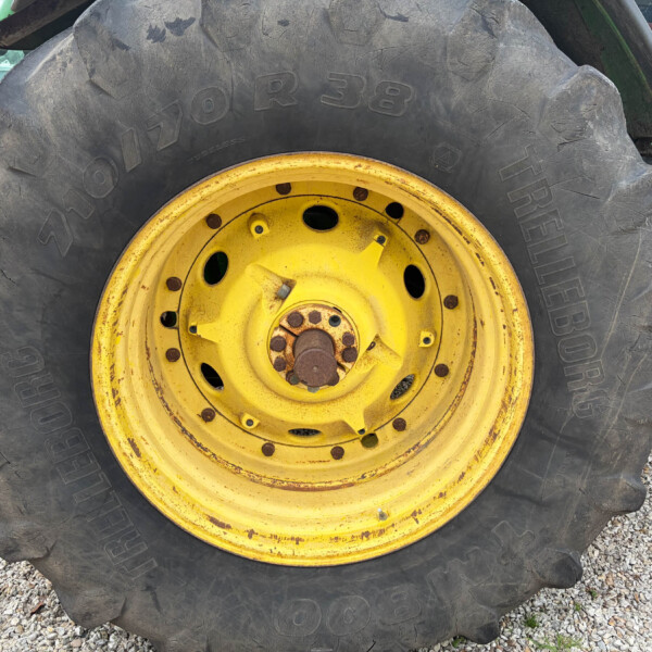 Close-up of a large tractor tire with a yellow rim, muddy tread, on gravel surface.