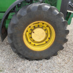 Close-up of a tractor rear wheel with a yellow rim on a gravel surface.