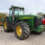 John Deere 8100 tractor with oversized rear tires in a gravel yard, a red tractor beside it.