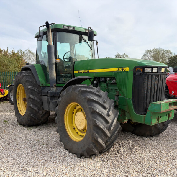 John Deere 8100 tractor with oversized rear tires in a gravel yard, a red tractor beside it.