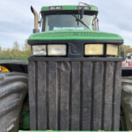 Close-up of a green tractor's front, showing large black grille, dual headlights, and oversized tires on either side.