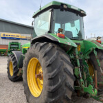 Close-up of a large green and yellow tractor parked outside a farm equipment showroom, with a New Holland Agriculture sign in the background.