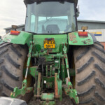 Rear view of a large green tractor with oversized tires and a yellow license plate reading P933 SRT, showing exposed machinery and hydraulic connections.