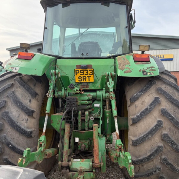Rear view of a large green tractor with oversized tires and a yellow license plate reading P933 SRT, showing exposed machinery and hydraulic connections.