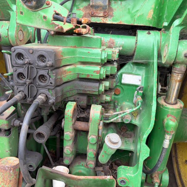 Close-up of a green hydraulic control block on a farming machine, showing hoses, bolts, and rust.