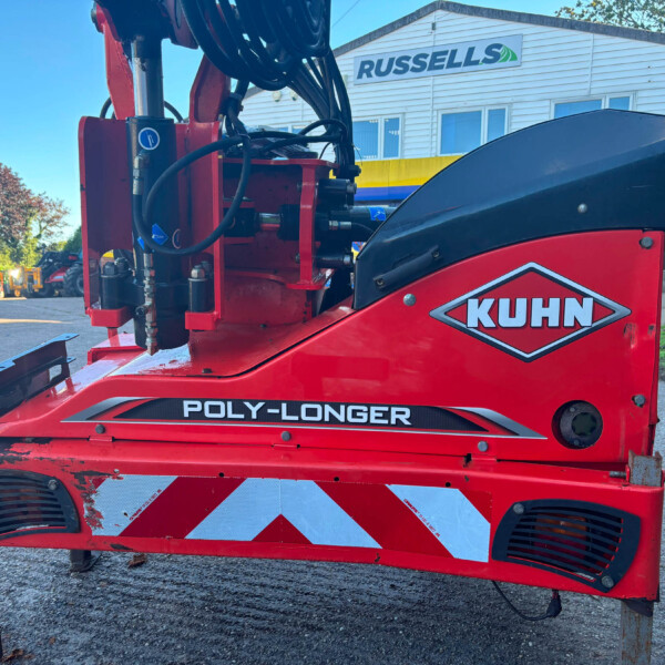 Close-up of red KUHN agricultural machine with hydraulic hoses and metal frame, 'POLY-LONGER' branding visible in foreground.