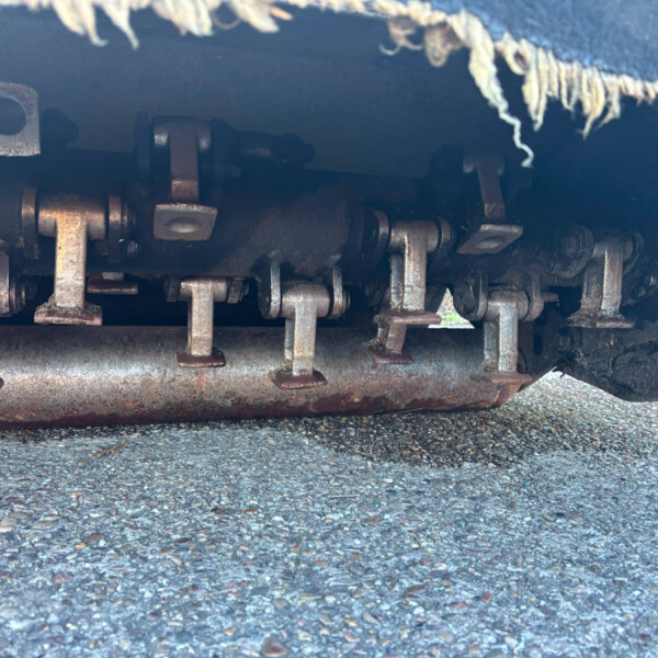 Rusty undercarriage of a train car with rusted hinges and brackets, visible on the trackbed beneath.