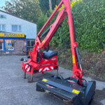 Red KUHN farming implement parked outside a Russell's store with blue and yellow signage and a hedge on the right side.