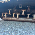Close-up of rusted metal drive chain and rollers under a heavy vehicle on a paved surface
