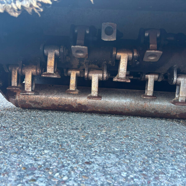 Close-up of rusted metal drive chain and rollers under a heavy vehicle on a paved surface