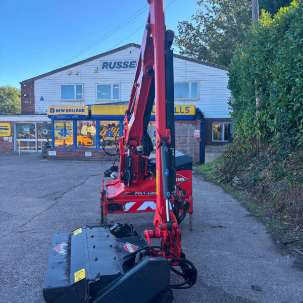 Red hydraulic agricultural machine with extended arms parked in front of a New Holland Agriculture storefront.