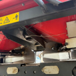 Red and black industrial machine frame with a yellow safety warning label showing multiple hazard icons and a person figure.