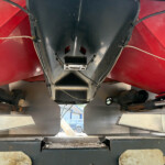 Underside view of red industrial equipment showing a metal frame, black center panel, and attached hoses/cables seen from below.