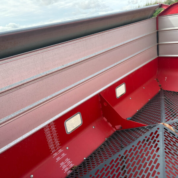 Close-up of a red truck trailer wall with silver trim, showing perforated metal stairs in the foreground and a height/load measurement chart on the side.