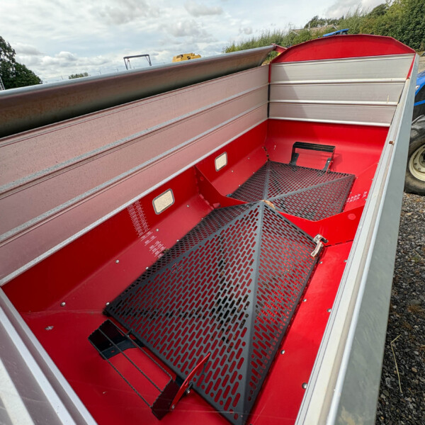 Red utility trailer interior with perforated metal ramp and seating steps, viewed from the open side, outdoors on gravel.