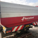 Rear of a red and gray Kverneland agricultural trailer on a gravel lot, brand text visible on the side.