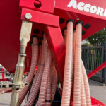 Close-up of red hydraulic machinery with multiple corrugated pink hoses and metal fittings outdoors.