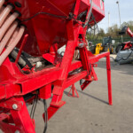 Close-up of red industrial machine frame with beige corrugated hoses and black cables in an outdoor yard.