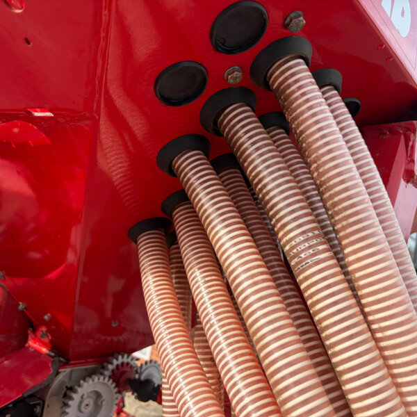 Close-up of red industrial machinery with multiple beige corrugated hoses connected to black fittings and gears visible in the background.
