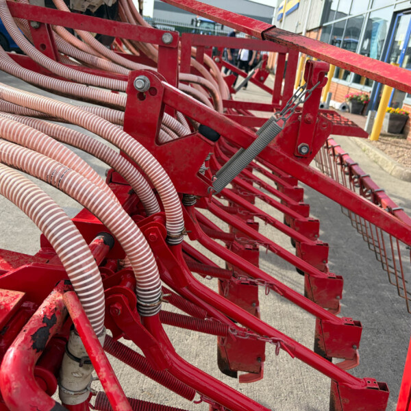 Close-up of red agricultural equipment with bundled flexible hoses and metal frames outdoors near a storefront.