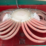 Round metal access hatch with numerous dusty orange hoses coiled around it inside a red-green industrial cabinet.