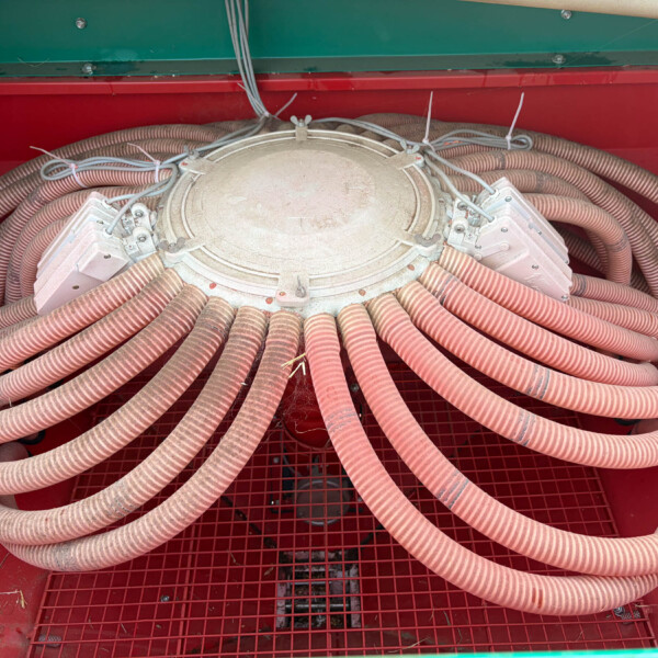 Round metal access hatch with numerous dusty orange hoses coiled around it inside a red-green industrial cabinet.