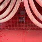 Close-up of flexible red hoses laid over a red metal grate in an industrial setting, with dust and debris nearby.