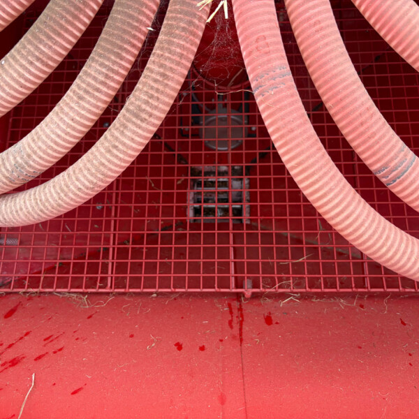 Close-up of flexible red hoses laid over a red metal grate in an industrial setting, with dust and debris nearby.