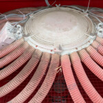 Dusty circular industrial lid surrounded by many red flexible hoses and electrical connectors.