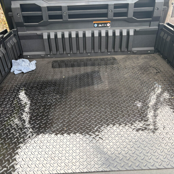 Diamond-plate truck bed with ribbed side walls and a small blue cloth in the left corner. It’s the cargo area of a rugged utility vehicle, viewed from above.