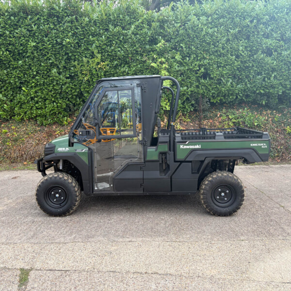 Green Kawasaki Diesel 4x4 utility vehicle parked on a paved surface with a tall green hedge in the background.